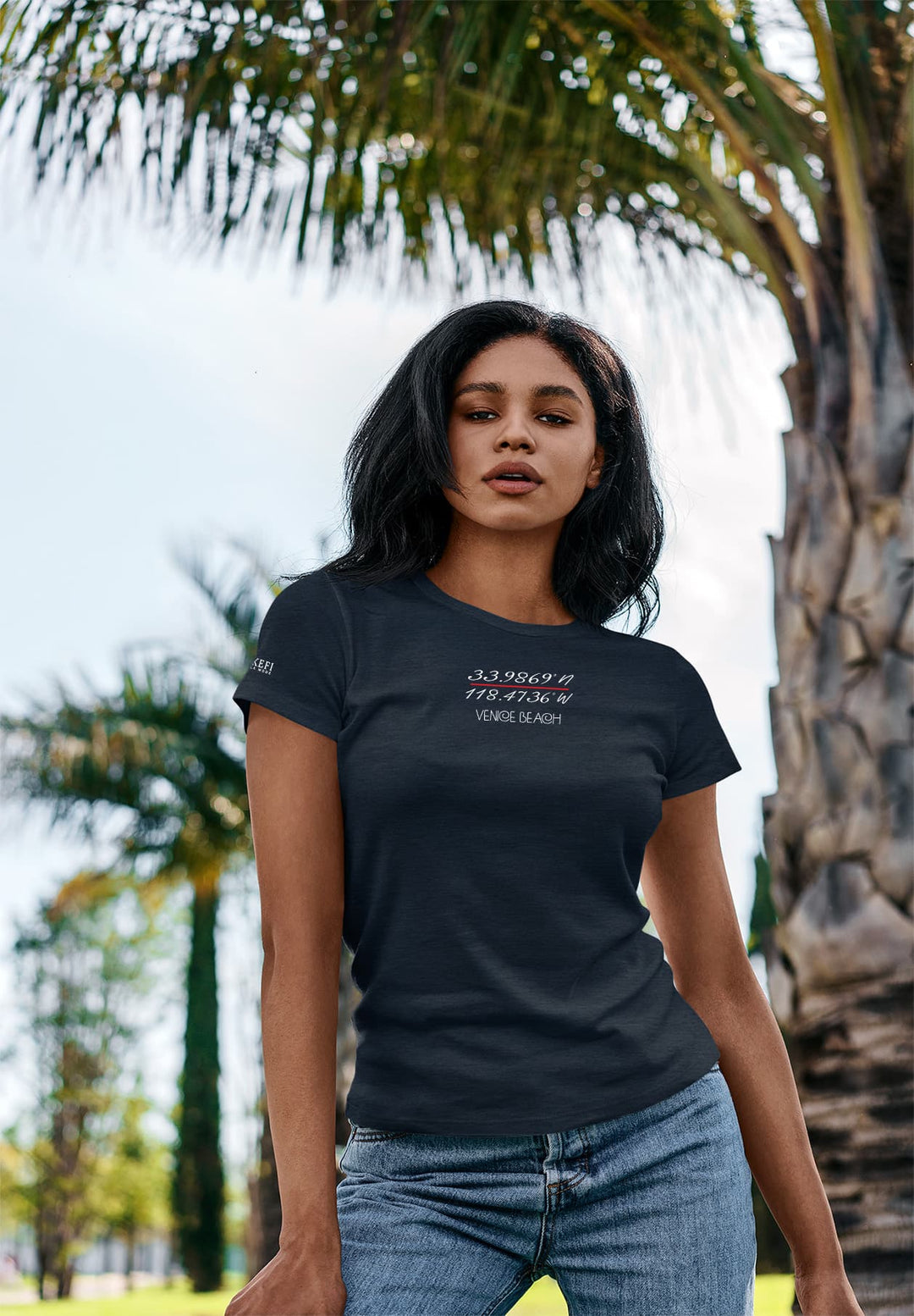 Surrounded by tall palm trees, she is wearing a blue T-shirt and appreciating the beauty of nature, blending in with the peaceful surroundings.