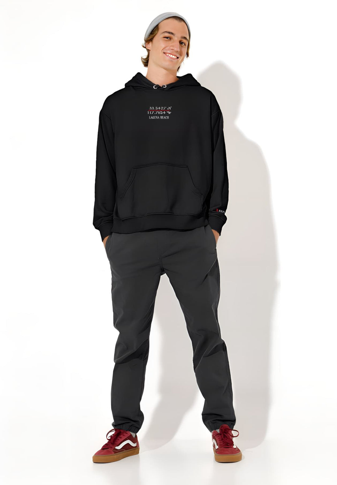 A man can be seen wearing a black hoodie and standing in front of a white wall.
