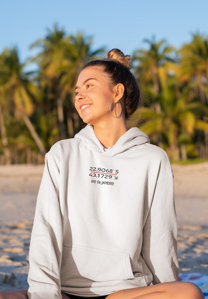 A young women who is smiling and wearing white sweatshirt while sitting on the beach.