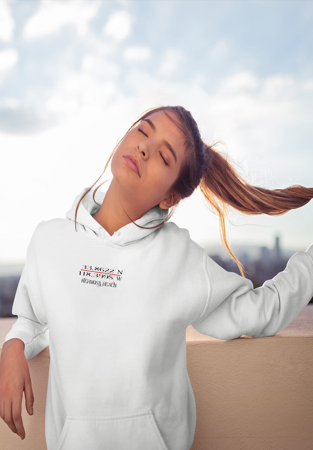 The young woman's relaxed posture against the wall in her white hoodie forms a stylish yet tranquil moment, etching a memory of modern simplicity.